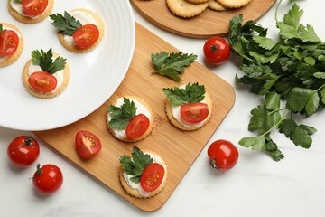 Tasty crackers with cream cheese, tomatoes and parsley on white table, flat lay