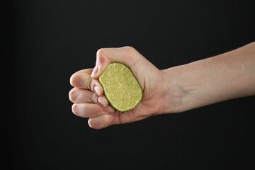 Woman squeezing lime on black background, closeup