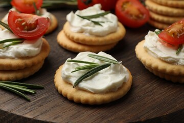 Tasty crackers with cream cheese, rosemary and tomatoes on wooden table, closeup