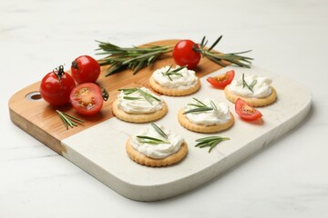 Tasty crackers with cream cheese, rosemary and tomatoes on white table, closeup