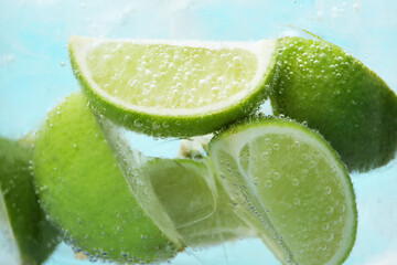 Refreshing soda water with slices of lime and ice in glass on light blue background, closeup