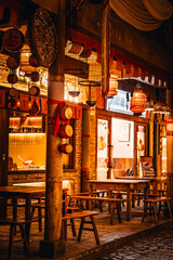 Warmly lit traditional Chinese shop street at night in Wangxian Valley Town, featuring wooden buildings, lanterns, and a cozy atmosphere under a large tree.