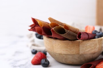 Tasty fruit leather rolls and berries on white marble table, closeup