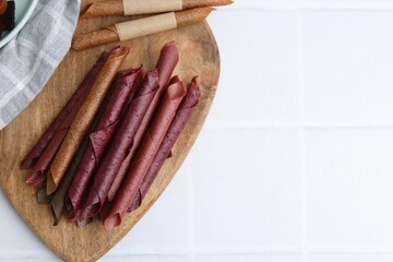 Tasty fruit leather rolls on white tiled table, flat lay. Space for text