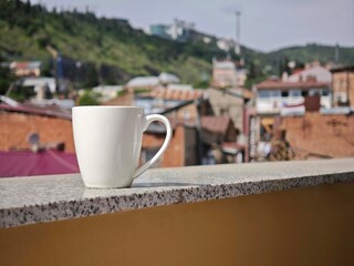 White mug standing on a balcony with Tbilisi cityscape in the background