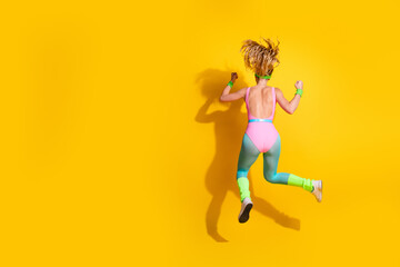 Energetic young woman in vibrant workout clothing jumping with joy against a bright yellow background, showcasing fitness