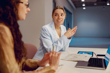 In a contemporary office environment, two skilled professional women are engaged in a discussion...