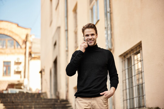 Handsome man strolling through city streets while engrossed in a phone call during bright daylight
