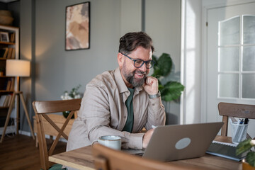 Smiling mature freelancer working from home office using laptop