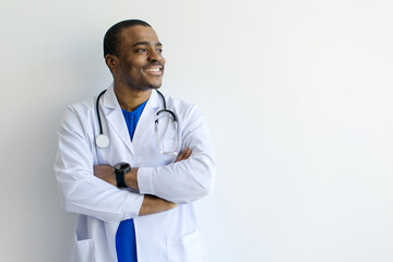 African American male doctor wearing white coat, standing with his arms crossed and looking...