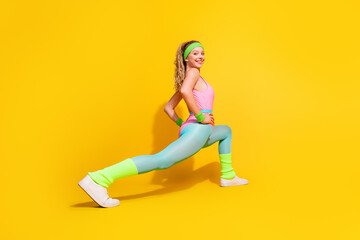Fototapeta premium Young woman in vibrant retro activewear stretching against yellow background showing fitness and happiness