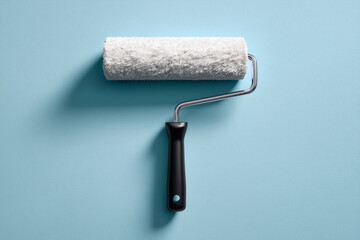Obraz premium Paint roller with a black handle sitting against a light blue backdrop, casting a subtle shadow.