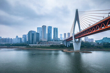 Modern city skyline and bridge over a wide river on an overcast day in Chongqing, China.