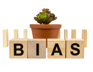 Wooden blocks spell "BIAS" in front of a potted succulent plant and upright dominoes.