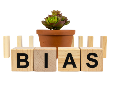 Wooden blocks spell "BIAS" in front of a potted succulent plant and upright dominoes.