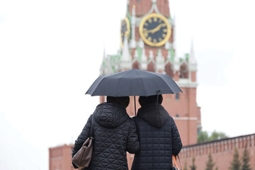 Two women with one umbrella standing on the Red Square in Moscow on Kremlin tower background