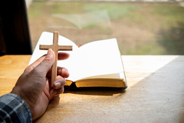 Young woman praying for blessings from God in front of Bible and cross which are symbols of faith...