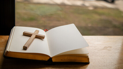 Cross and Bible placed on the table by the window symbolizing faith and devotion to God, preparing to learn God's teachings from the Bible.Concept of praying for blessings from God with faith.