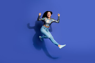 Fototapeta premium Young woman in a stylish holographic outfit jumping excitedly against a vibrant purple background, radiating energy and joy