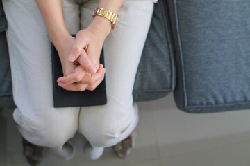 young woman put her hands together and placed them on her Bible to pray alone in her home for God's blessings. With faith and power of faith in God, young woman laid her hands on Bible in prayer.