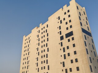 Fototapeta premium White Color Commercial Residential Building Complex with Black Color Windows And Blue Sky Background. Highrise Skyscraper Building Exterior Outdoor Full View. G+10 floor Tallest Skyline With PentHouse