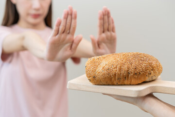 Gluten allergy, asian young woman hand push out, refusing to eat white bread loaf on plate in...