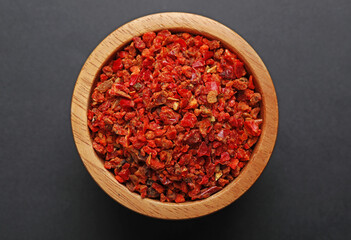 Red chili pepper flakes in bowl on dark table, top view