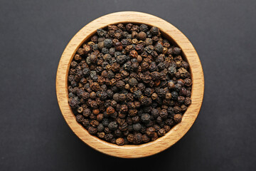 Aromatic peppercorns in bowl on dark table, top view