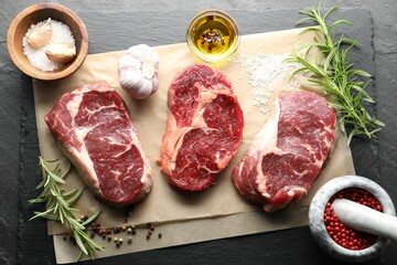 Pieces of raw beef meat and spices on black table, flat lay