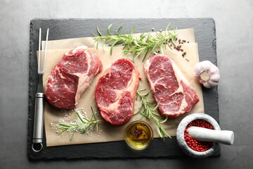 Pieces of raw beef meat, spices and carving fork on grey table, flat lay