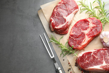 Pieces of raw beef meat, spices and carving fork on grey table, flat lay. Space for text