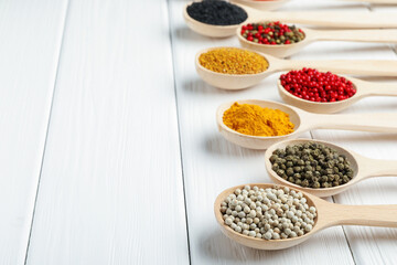 Different aromatic spices in spoons on white wooden table, closeup. Space for text