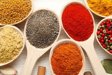 Different aromatic spices in spoons on white wooden table, flat lay