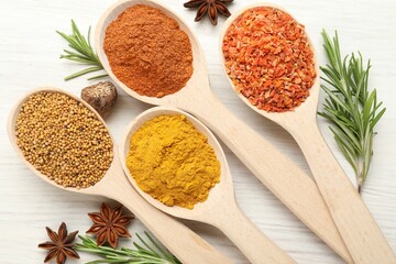 Different aromatic spices in spoons on white wooden table, flat lay