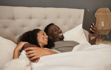 Smiling multiracial couple using a tablet in their bed