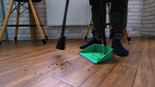 Sweeping dirt off a tiled floor with a broom. A man cleaning an apartment, slow motion.