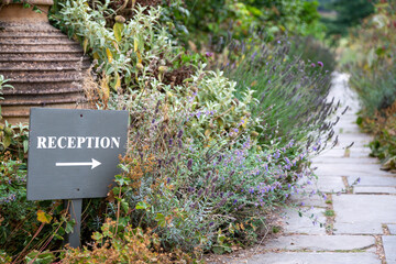 A tranquil reception pathway marked by a grey arrow sign leads through lavender-lined stone slabs into a peaceful garden.