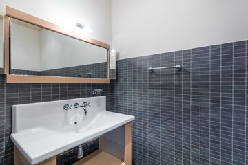 Laconic design of the bathroom, decorated with gray tiles. A mirror over a white sink.