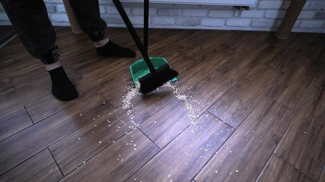 Oatmeal spilled on the floor. Sweep up dirt with a broom, dustpan, top view. A man cleans an apartment. Slow motion.