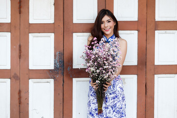 Beautiful Asian chinese woman in traditional cheongsam smiling, posing with a large bunch of fresh spring flowers against a classic wooden door.