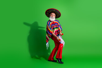 Charismatic elderly man in traditional Mexican outfit with vibrant poncho and sombrero posing joyfully against a green background