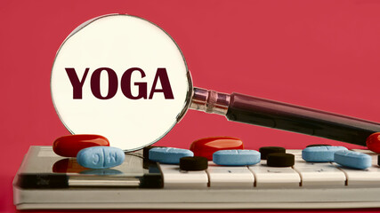 The word YOGA written through a magnifying glass on a calculator with pills on it on a red background with a white spot from a magnifying glass