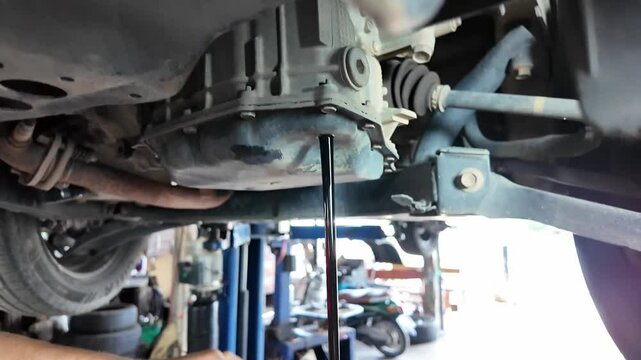 Automotive Fluid Change,A mechanic drains fluid from a car's gearbox,A hand carefully removes the drain bolt while a pan waits to collect the used fluid.