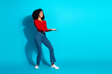 Attractive young woman in casual outfit posing against a vibrant blue background while showing a welcoming hand gesture.