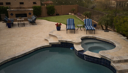 an aerial view of a desert landscaped backyard featuring a travertine tiled pool deck, putting green, outdoor kitchen and fireplace.