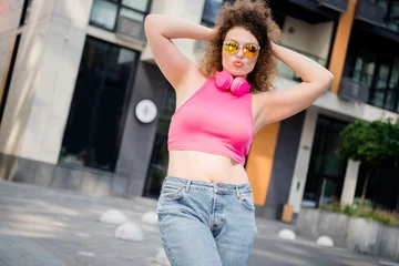 Gordijnen Trendy young woman enjoying a casual summer day outdoors in the city, wearing stylish jeans and a pink top © deagreez