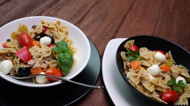 Piatti con pasta fredda condita con olive, pomodori, sottaceti, mozzarelle, basilico e prezzemolo