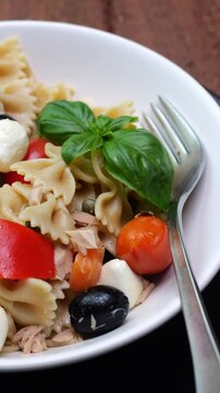 Primo piano di un piatto con pasta fredda condita con olive, pomodori, mozzarelle, sottaceti e basilico, video verticale