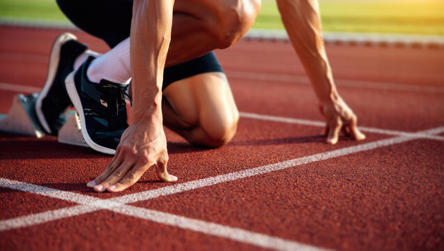 Closeup muscular legs and hands of an athlete in starting position on red running track. Runner on the race arena ready to start the sprint. Focus, readiness and determination before the quest begins