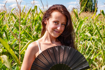 Happy woman with smiling face portrait hold black flamenco summer fan in hot cornfield, geisha...